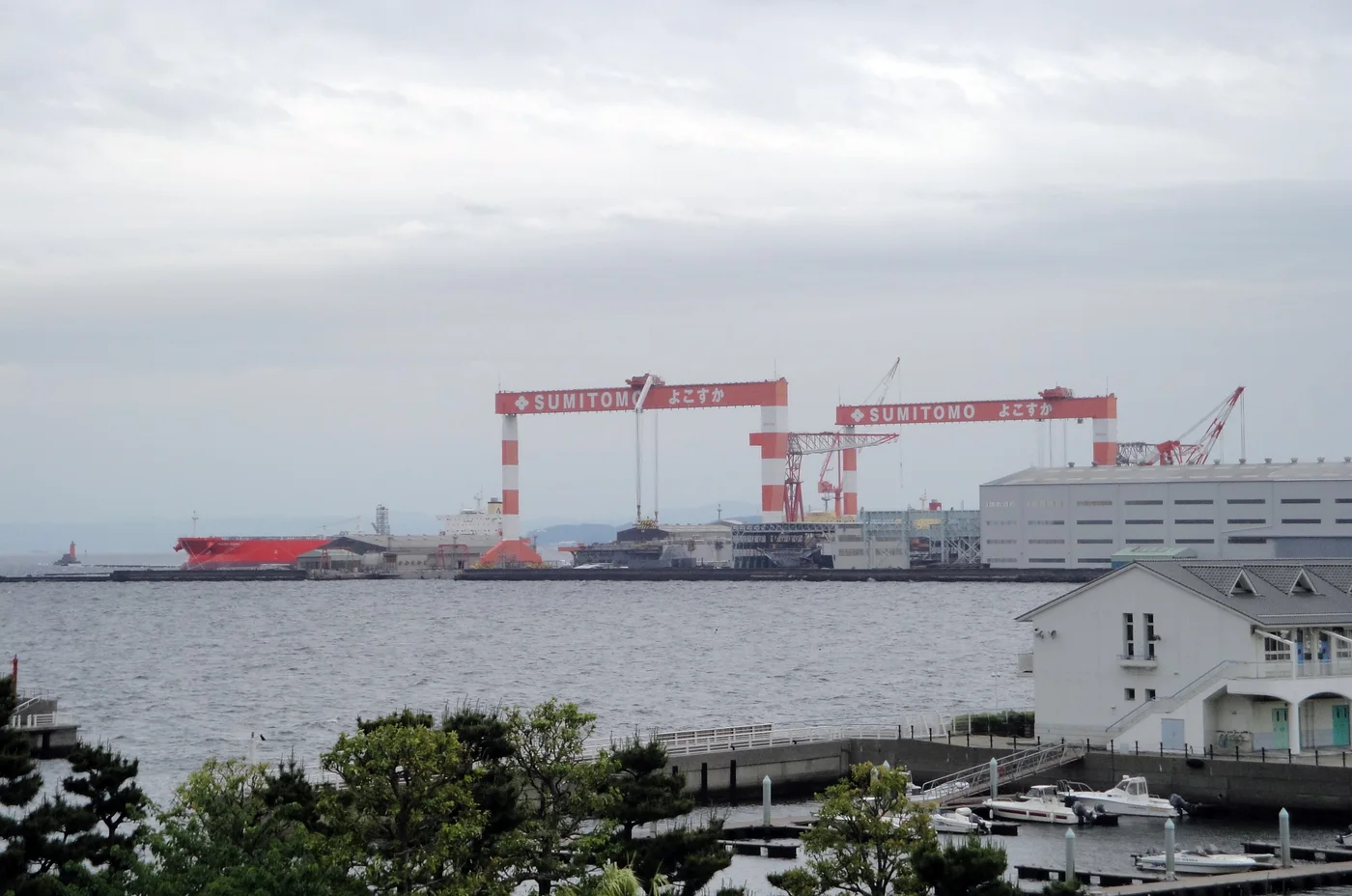 Red Sumitomo gantry cranes and a vessel at the Yokosuka shipyard
